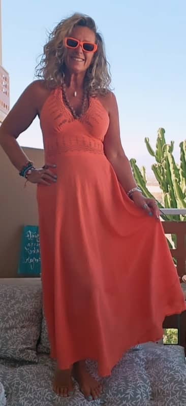 Mujer sonriente posando con vestido largo de color naranja coral de estilo boho chic, confeccionado en algodón 100% con escote halter y cuerpo bordado.