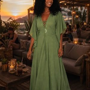 Mujer sonriente con pelo rizado viste un vestido largo verde de algodón de India con mangas mariposa y escote acordonado en una terraza al atardecer.