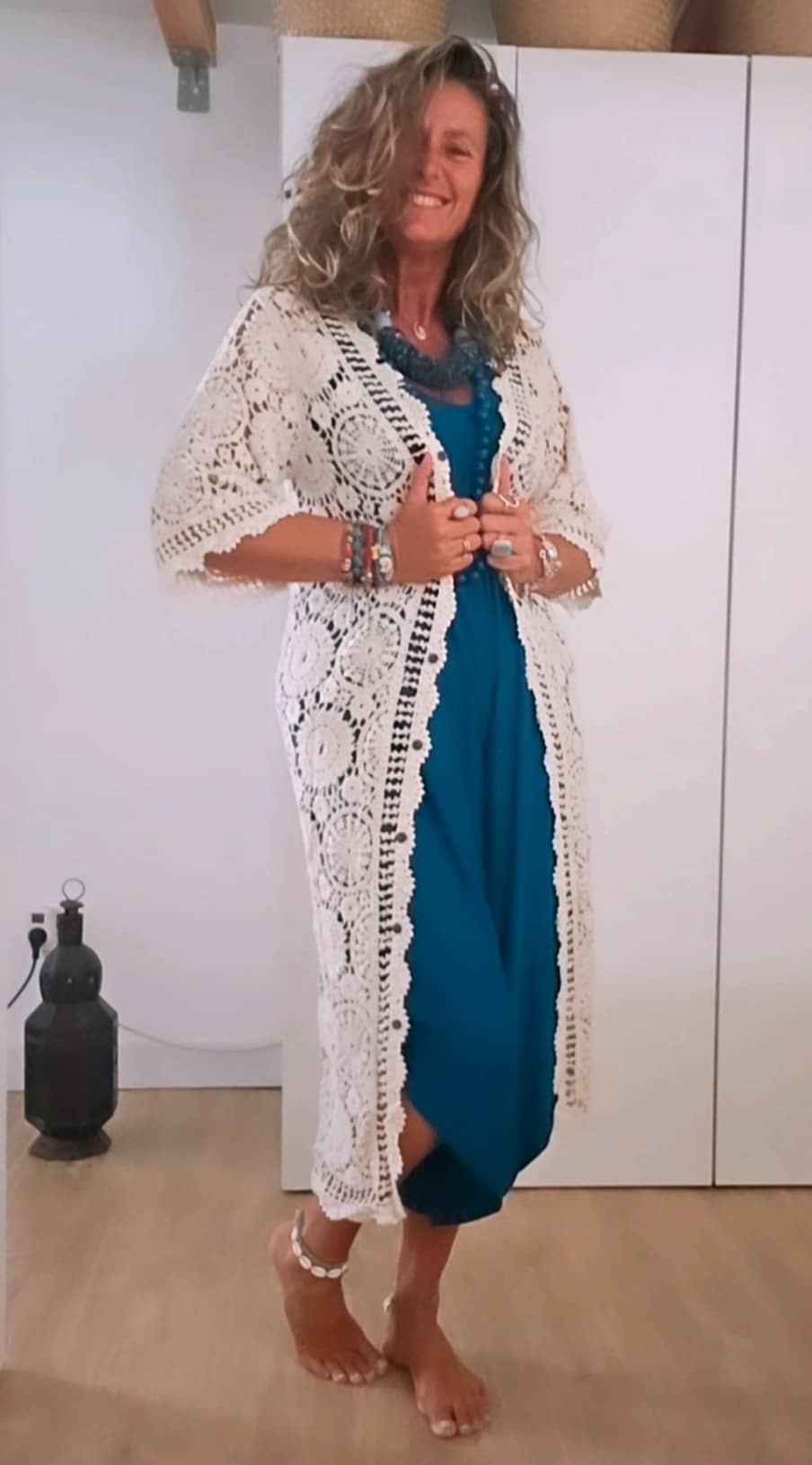 Modelo vistiendo un kimono largo calado de ganchillo sobre un mono azul con collares de estilo hippie