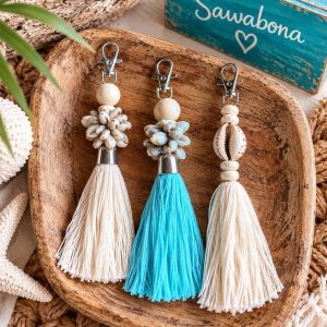Llaveros artesanales de conchas y borlas de algodón en color blanco y azul turquesa estilo boho chic sobre plato de madera de Sawabona.