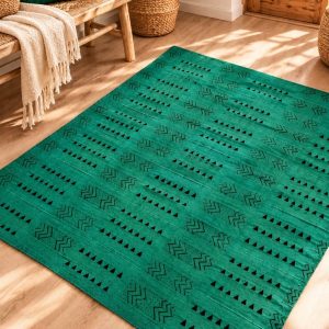 Alfombra de bogolán auténtico en color verde esmeralda con estampados geométricos étnicos sobre un suelo de parqué en un salón de estilo bohemio.