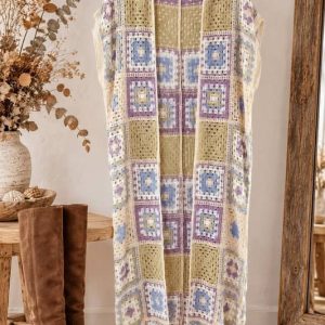 Chaleco largo de crochet calado estilo granny square en tonos pastel colgado de una percha junto a botas camperas de ante marrón en la tienda online Sawabona.