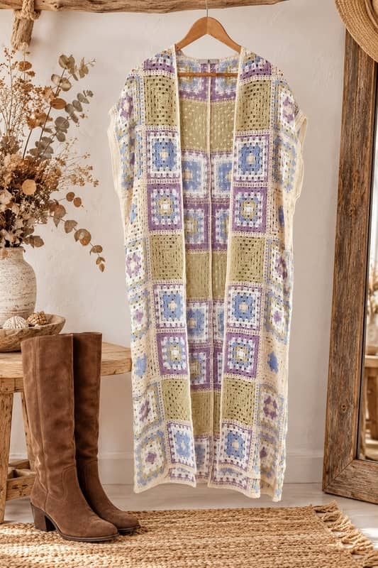 Chaleco largo de crochet calado estilo granny square en tonos pastel colgado de una percha junto a botas camperas de ante marrón en la tienda online Sawabona.