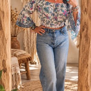 Mujer vistiendo top boho chic con estampado floral azul y rosa, mangas acampanadas y pantalón vaquero de talle alto frente a un espejo.